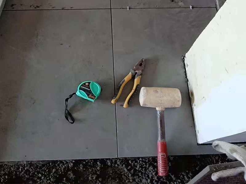 客廳地磚鋪貼：鋪貼的工具包括橡膠錘和粘結(jié)劑。在進(jìn)行施工之前先把所需要的這些材料都整理好放在一旁備用；基層的處理工作對(duì)瓷磚的平整度有很大的影響，對(duì)于基層要做好清潔工作，還有找平工作。放樣：在進(jìn)行瓷磚的鋪貼工作之前還事先找好垂直線，這樣可以在鋪貼的時(shí)候找到瓷磚的水平線，讓瓷磚鋪貼的更加的平整。粘結(jié)劑加水?dāng)嚢杈鶆?，靜置10分鐘之后就可以使用。將瓷磚表面的浮灰清除，再在瓷磚背面均勻的涂抹上粘結(jié)劑，按照預(yù)鋪的順序?qū)⒋纱u鋪貼在地面上，最后用橡膠錘輕輕拍打至服帖齊整。